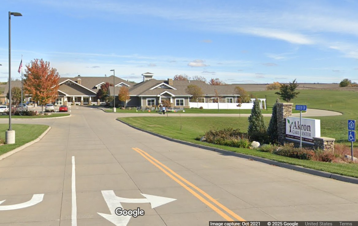 The street view of the exterior of the Akron Care Center, a sprawling grey one-story building.
