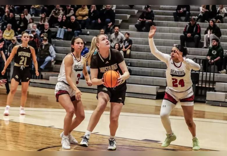 Nielsen stands with the ball in her hand, while looking up at the hoop. She is standing just inside the 3-point line, with an opponent on either side of her.
