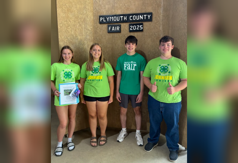 The group stands under a "Plymouth County Fair 2025" sign. The girl on the far left is holding the ribbons, and the boy on the far right is giving the thumbs-up sign.