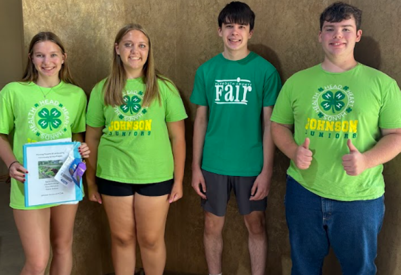 The group stands under a "Plymouth County Fair 2025" sign. The girl on the far left is holding the ribbons, and the boy on the far right is giving the thumbs-up sign.