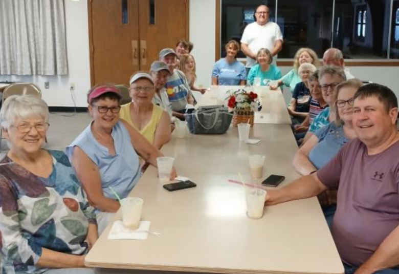 About a dozen people sit on both sides of a long, rectangular table, enjoying their root beer floats.